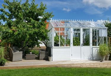 Miljøbillede af drivhuset Gothic 236, hvor drivhuset er placeret på et træterrasse og fyldt med planter