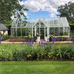 Billede af drivhuset Victoria, placeret i en have fyldt med planter